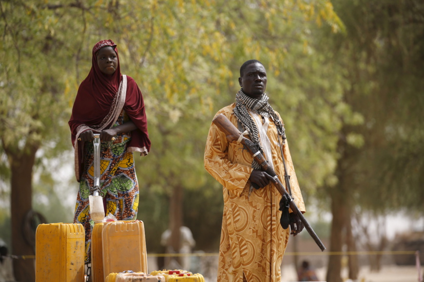 Un membre d'un groupe d'autodéfense civil tient un fusil de chasse tandis qu'une femme pompe de l'eau dans des jerrycans à Kerawa, Cameroun, 16 mars 2016. © REUTERS/Joe Penney