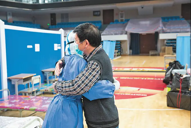 A cured coronavirus patient hugs a medic who has taken care of him during his treatment in the Wuchang Fangcang hospital, before the hospital closes, March 10, 2020. Photo by Zhang Wujun, People’s Daily