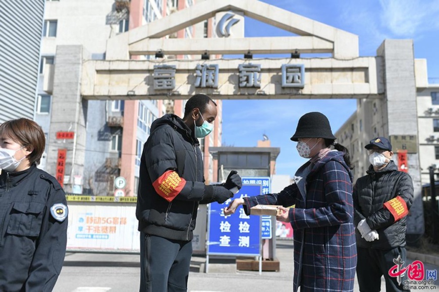 Ali Albade takes body temperature for a resident at the entrance of his community, March 10. Photo by Zhang Ruomeng, China.com.cn