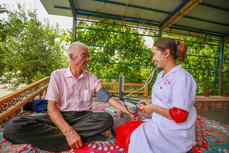 Photo shows a volunteer, who is also a member of Communist Party of China (CPC), measuring blood pressure of a senior citizen in Ershilidian village, Ershilidian township, Hutubi county, Changji Hui autonomous prefecture, northwest China’s Xinjiang Uygur autonomous region, July 22. Photo by Tao Weiming/People’s Daily Online