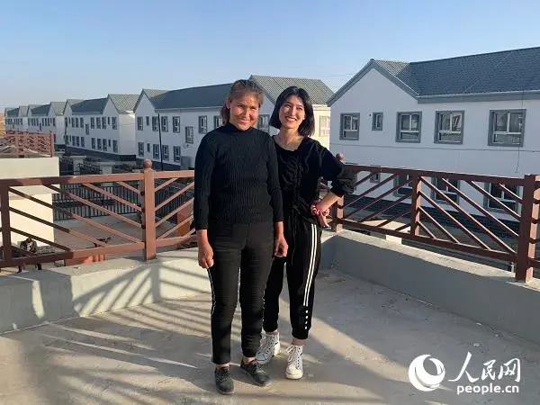 Kuwahan Mettursun and her daughter pose for photos in front of their new home. (Photo by Yang Rui/People’s Daily Online)