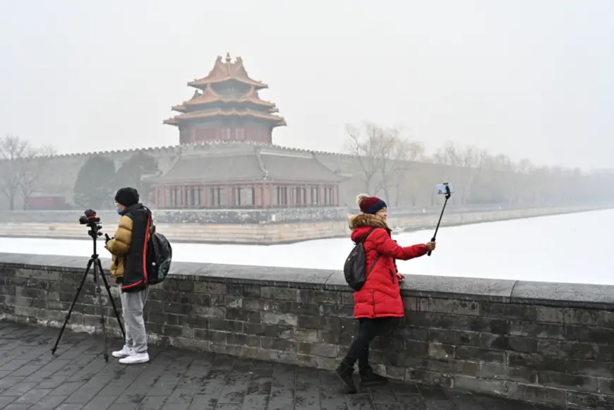 Tourists take photos in front of a snow-covered corner tower of the Forbidden City, a site along the Central Axis of Beijing that will apply for UNESCO World Heritage status, Jan. 25. (Photo by Li Xin/Xinhua News Agency)