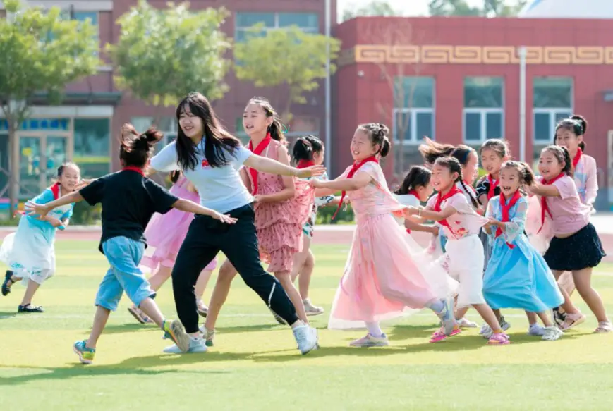 A volunteer, also a college student, plays games with children at a school in Yuquan district, Hohhot city, north China’s Inner Mongolia autonomous region, July 14, 2021. (Photo by Ding Genhou/People’s Daily Online)