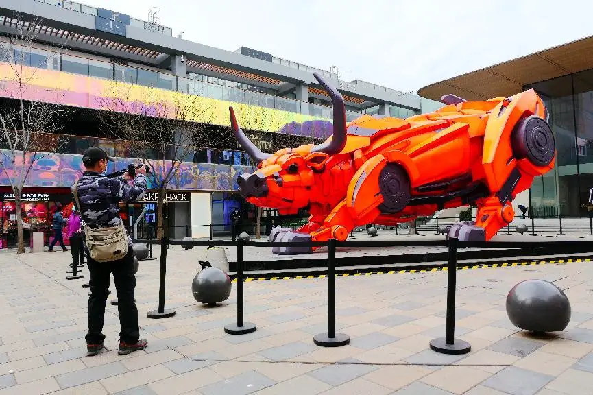 A tourist takes pictures of a large sculpture featuring a mechanical bull at Sanlitun in Chaoyang district, Beijing, Feb. 21, 2021. (Photo by He Luqi/People’s Daily Online)