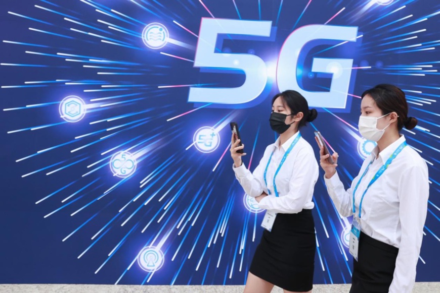 Photo taken on Sept. 27, 2021 shows two girls passing by a poster of PT Expo China 2021, an influential information and communications technology (ICT) annual event in Asia, held in Beijing. (Photo by Chen Xiaogen/People’s Daily Online)