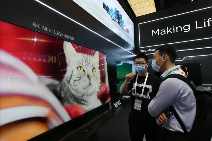 A staff member introduces a smart 8K television to a visitor at the 2021 World UHD Video Industrial Conference held in Guangzhou , south China's Guangdong province, May 10, 2021. (Photo by Xu Jianmei/People's Daily)