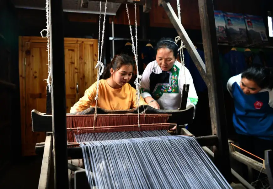 Long Laoxiang (middle), a master of Miao embroidery, teaches a college graduate apprentice to weave cloth with a handloom in Zila village, Shilan township, Huayuan county, Xiangxi Tujia and Miao autonomous prefecture, central China’s Hunan province, April 29, 2020. (Photo by Long Enze/People’s Daily Online)