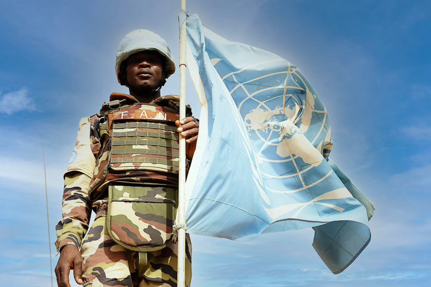 Un Casque bleu nigérien pose devant le drapeau des Nations Unies à Ménaka, dans le sud-est du Mali. © MINUSMA/Harandane Dicko