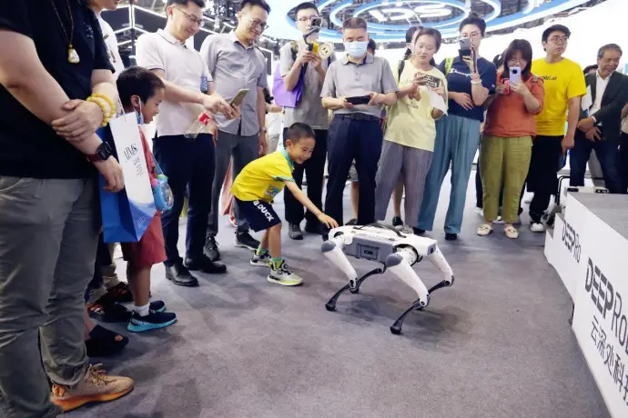 A boy plays with a robotic dog at the 2023 World Artificial Intelligence Conference in Shanghai, July 6. (Photo by Chen Yuyu/People's Daily Online)