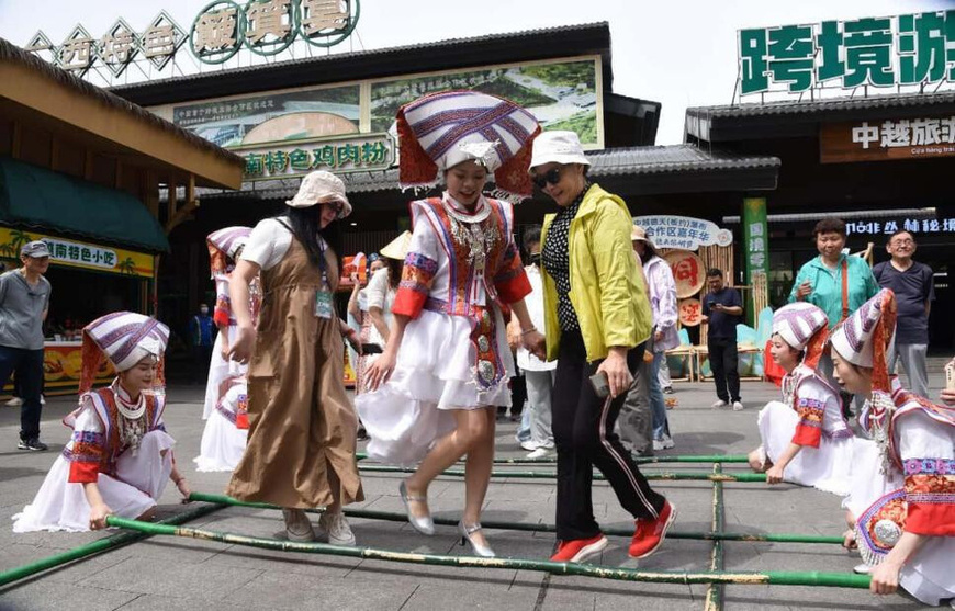 Tourists join a bamboo pole dance performance at the China-Vietnam Detian-Ban Gioc Waterfall cross-border tourism cooperation zone. (Photo courtesy of the media center of Daxin county)