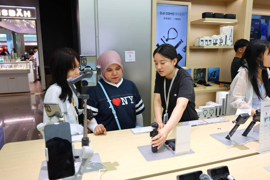 A sales assistant explains the features of a Chinese gimbal camera to foreign travelers at a duty-free mall in Sanya, south China's Hainan province. (Photo/Zhang Yuanming)