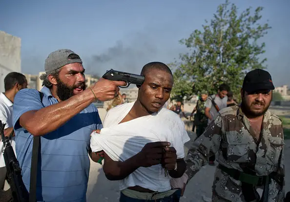 Un milicien libyen pointe son pistolet sur la tête d'un migrant. Crédits photo : sources