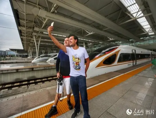Foreign passengers take photos with the Fuxing bullet train. (Photo by Wang Chu from People’s Daily Online)