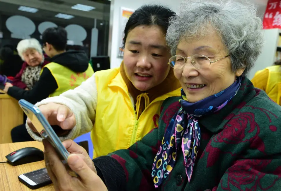 An 80-year-old woman named Ge Yuqi is learning how to use social application WeChat with the help of a volunteer on January 16, 2018. (Photo by Shi Yucheng from People’s Daily Online)