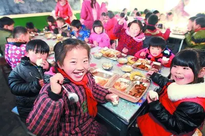 Left-behind children, whose parents have left rural areas to become migrant workers in towns or cities, enjoy their free lunch in the school canteen in central China’s Anhui province. (Photo from People’s Daily Online)