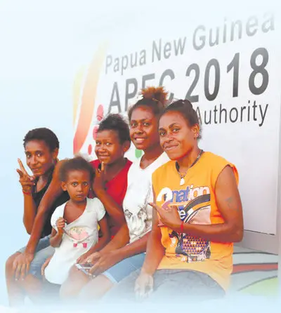 PNG citizens pose for pictures by an advertising board of APEC. Photo from Xinhua News Agency