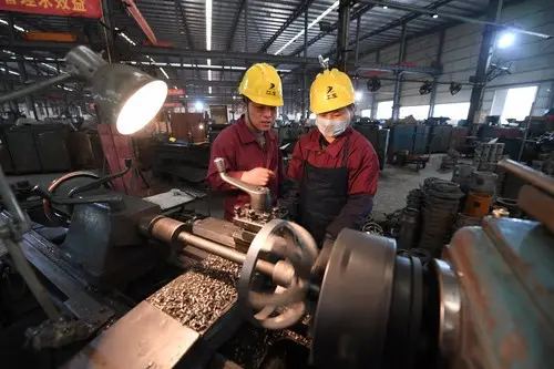 On February 25, 2019, Chen Ganfei, deputy to the National People’s Congress and team leader of a lathe group in Jiangxi Gas Compressor Company, communicate with a co-worker over production techniques. (Photo by People’s Daily)
