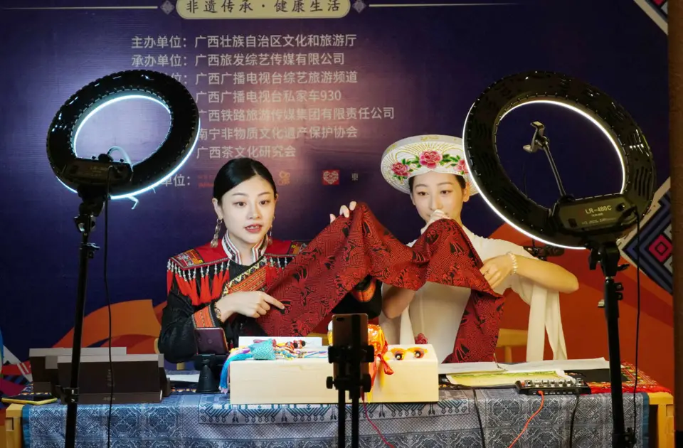 Two women of ethnic minority groups in Nanning, capital of south China’s Guangxi Zhuang Autonomous Region, promotes Zhuang brocade, a cultural creative ICH product during the first ICH-themed shopping festival held in the city, June 6. (Photo by Yu Xiangquan/ People’s Daily Online)