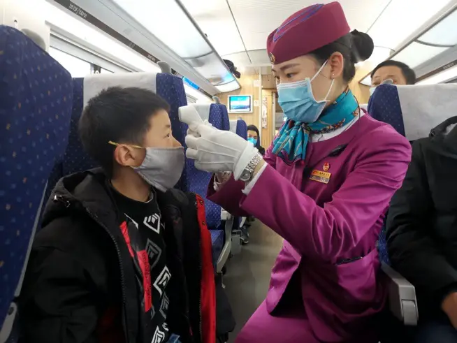 A car attendant checks body temperature of a boy passenger during the Spring Festival travel rush on Feb. 2, 2020. Photo by Hu Zhiqiang/People’s Daily Online