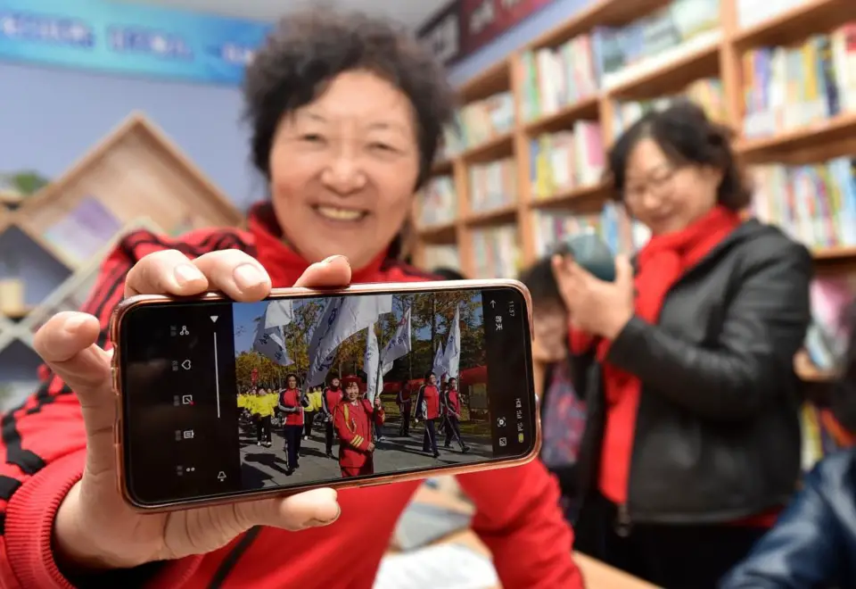 A female citizen who has learnt how to shoot videos with smart phone shows a video of her life after retirement in a community bookstore in Hanjiang district, Yangzhou, east China’s Jiangsu province, Nov. 12, 2020. (Photo by Zhuang Wenbin/People’s Daily Online)