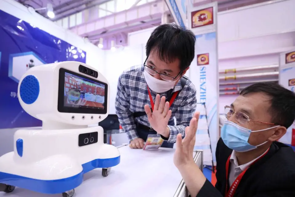 A staff member (right) demonstrates a companion robot that can perform tasks including measuring temperature, helping with study, and keeping the user company at the 8th China SME Investment and Financing Expo in Beijing, Oct. 10, 2020. (Photo by Chen Xiaogen/People’s Daily Online)