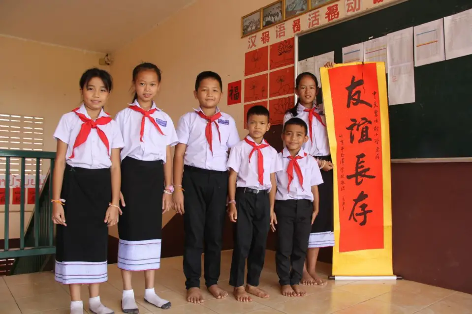 Students of the China-Laos Friendship Nongping Primary School in Laos pose for a picture with a calligraphy work sent by a primary school in Beijing in May 2019. The calligraphy work says "Long live our friendship." (Photo by Sun Guangyong/People's Daily)
