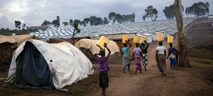 Des femmes retournent dans leurs abris sur le site de déplacés de Plaine Savo dans la province d’Ituri après avoir récupéré de l’eau. © UNHCR/Hélène Caux