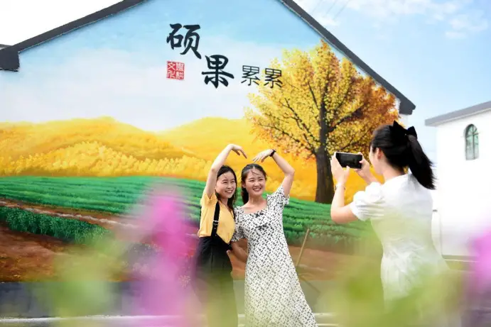 Visitors pose for pictures in front of a wall painting in Huangjindian village, Tancheng county, Linyi, east China's Shandong province. (Photo by Fang Dehua/People's Daily Online)