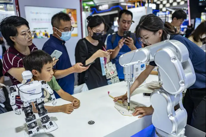Visitors watch a robotic arm do traditional Chinese calligraphy on a fan at the 2023 World Artificial Intelligence Conference in Shanghai, July 6. (Photo by Wang Chu/People's Daily Online)