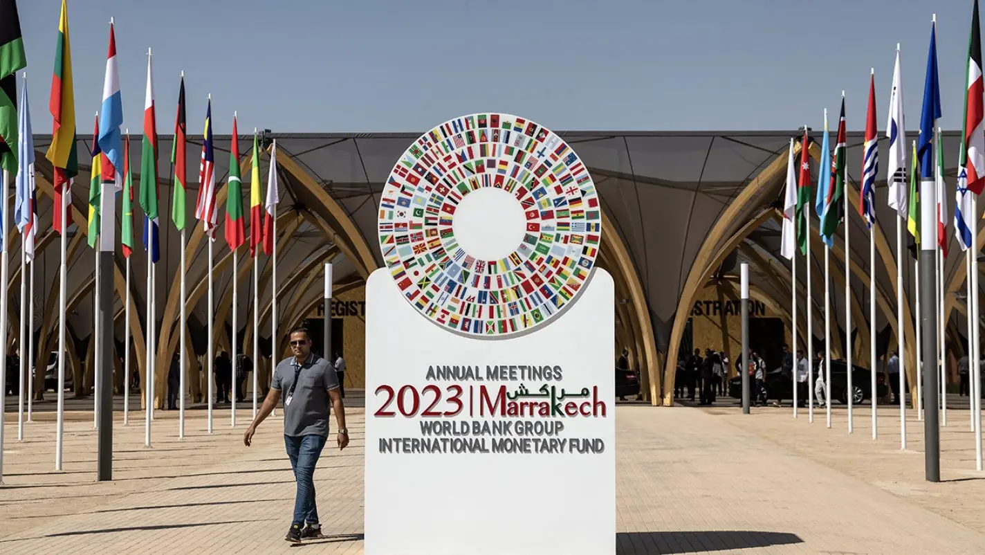 Un homme passe devant l'emblème des réunions annuelles 2023 du FMI et de la Banque mondiale à Marrakech. Photo : FADEL SENNA / AFP)