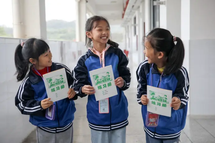 Students of an elementary school in Xunwu county, Ganzhou city, east China's Jiangxi province, display exercise books made from cardboard boxes recycled by Cainiao, the logistics arm of China's e-commerce giant Alibaba Group. (People by Zhang Jie)