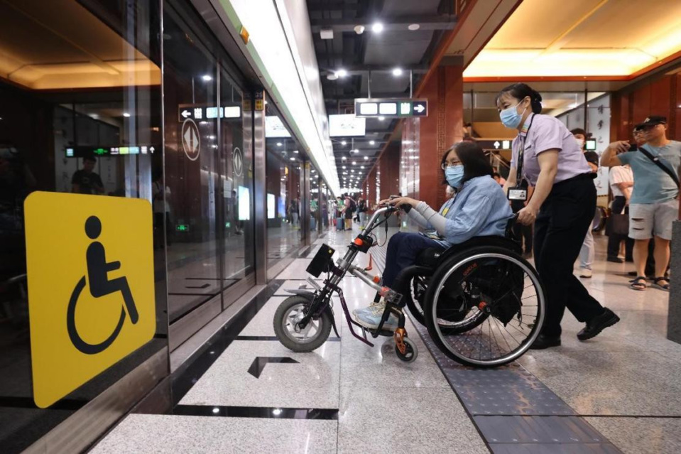 A metro staff member helps a passenger in a wheelchair board a train in Beijing. (Photo by Chen Xiaogen/People's Daily Online)