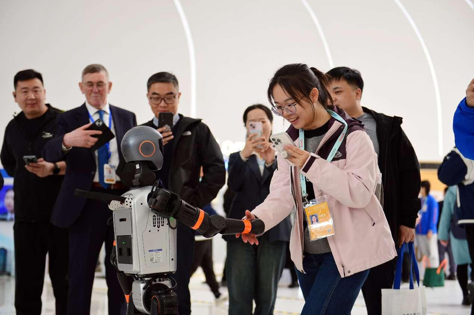 A journalist shakes hands with a robot at the 2025 Zhongguancun (ZGC) Forum Annual Conference in Beijing. (Photo by Chen Bin/People's Daily)