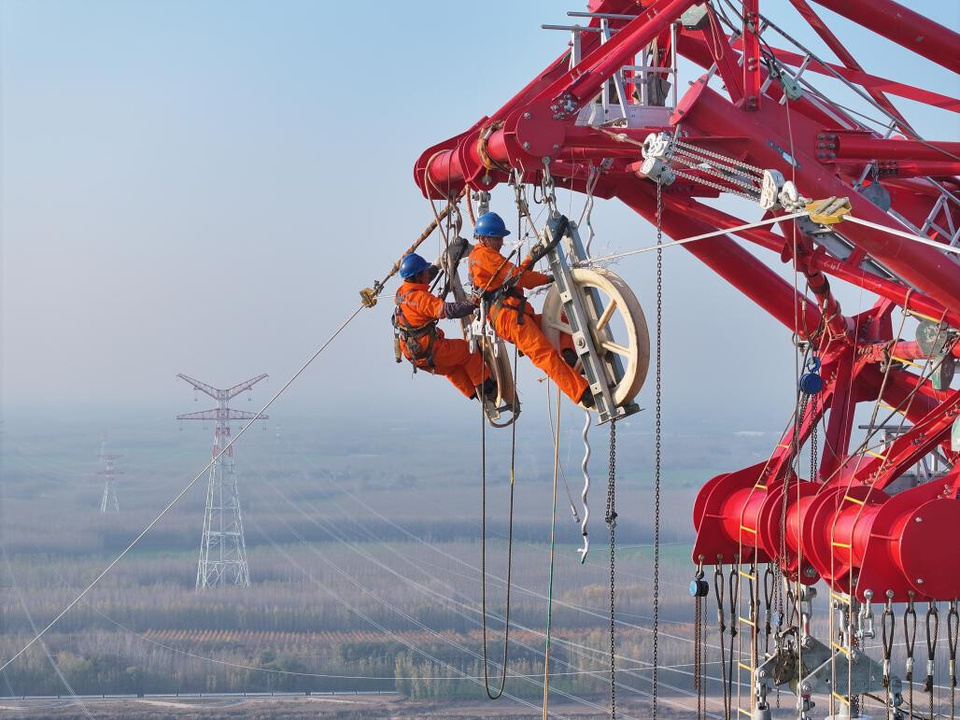 Workers work on a transmission tower in the Shandong section of the Longdong-Shandong ±800 kilovolt direct current (DC) transmission project. (Photo by Xu Ke/People's Daily Online)